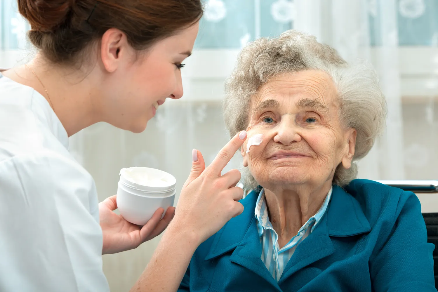 SENIOR GOLD 24 GMBH, Krankenschwester trägt Creme auf das Gesicht einer alten Dame auf